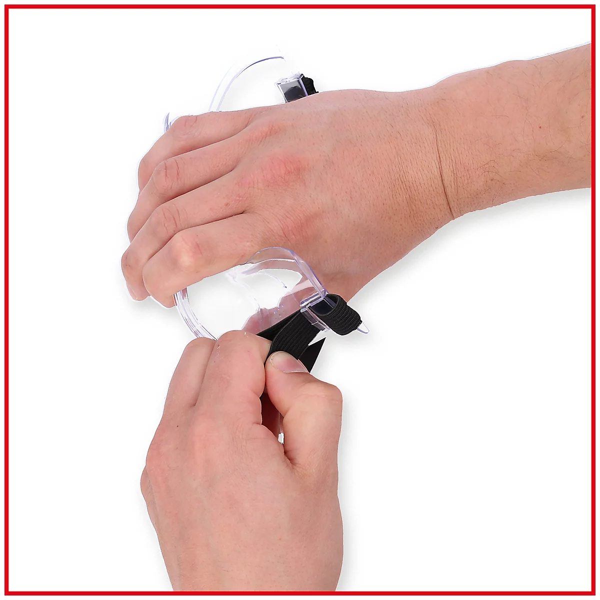 Hände halten eine transparente Schutzbrille mit schwarzem Band und Nadel. Der Arm ist im Hintergrund zu sehen.